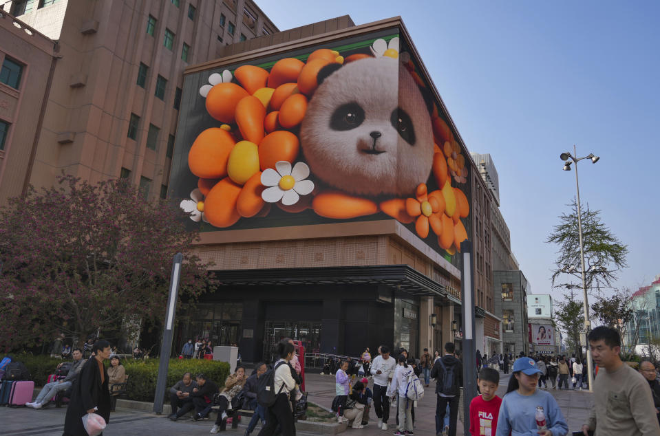 En un centro comercial de Pekín (China), el viernes 5 de abril de 2024, varias personas se sientan junto a un cartel en el que aparece un dibujo animado de un panda. (AP/Tatan Syuflana)
