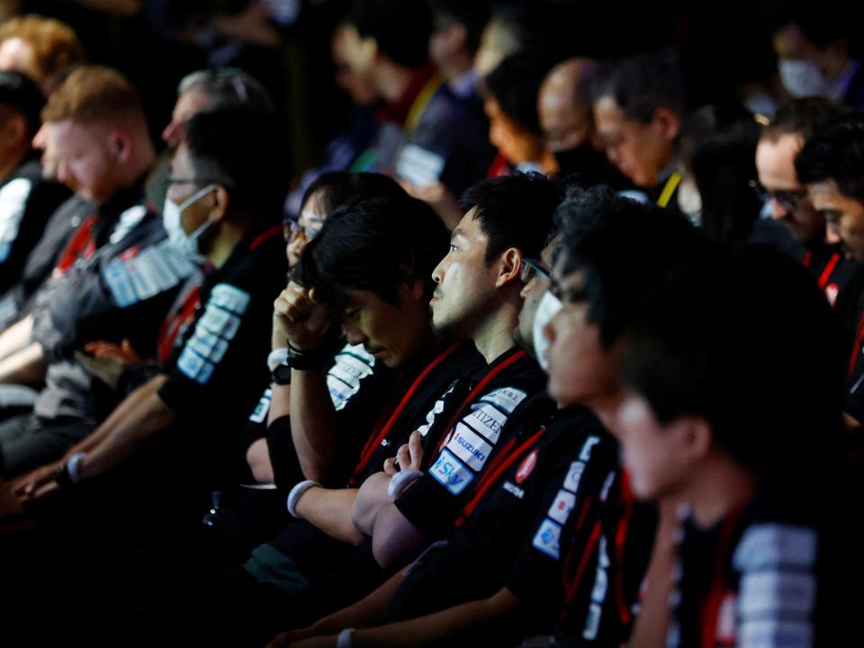 people sitting in rows in a dark room with tense faces wearing matching black shirts with white symbols on the arms