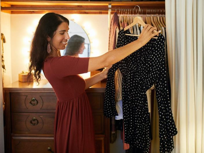 A woman looks at a dress in her closet.