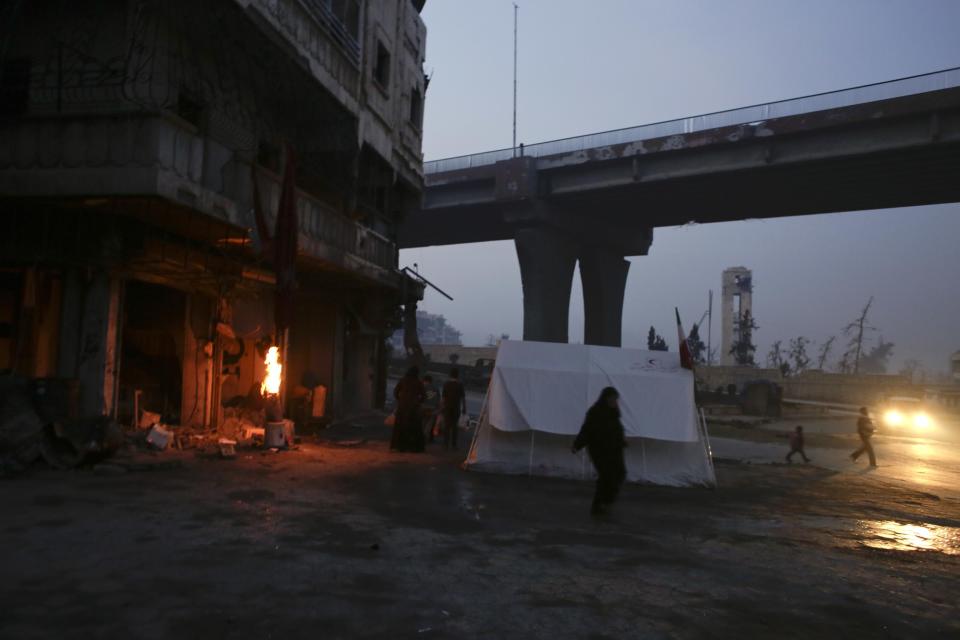 People warm up next to a fire outside their tent as others return to their houses at the once rebel-held Sakhour neighborhood in the eastern Aleppo, Syria, Tuesday, Jan. 17, 2017. Parts of the once rebel-held eastern neighborhoods in the northern Syrian city of Aleppo are returning to normal nearly three weeks after opposition fighters left the city to the suburbs. (AP Photo/Hassan Ammar)