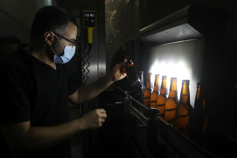 A worker holds a bottle of beer inside a beer factory in Mazraat Yachouh