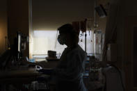 FILE - In this Nov. 19, 2020, file photo, registered nurse Virginia Petersen works on a computer while assisting a COVID-19 patient at Providence Holy Cross Medical Center in the Mission Hills section of Los Angeles. U.S. hospitals slammed with COVID-19 patients are trying to lure nurses and doctors out of retirement and recruiting nursing students and new graduates who have yet to earn their licenses. (AP Photo/Jae C. Hong, File)