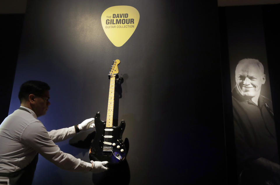 FILE - In this March 27, 2019, file photo, a technician arranges 'The Black Strat' from the collection of David Gilmour, guitarist, singer and songwriter of Pink Floyd, during a press opportunity at Christie's auction rooms in London. Christie’s auction house says it raised $21.5 million Thursday, June 20, 2019, selling off more than 120 guitars owned by the Pink Floyd guitarist, singer and songwriter. Proceeds went to ClientEarth, a non-profit fighting climate change. A black Stratocaster, dubbed the “Black Strat”, was the top item and was snatched up for $3,975,000, a new world record for a guitar at auction. (AP Photo/Kirsty Wigglesworth, File)