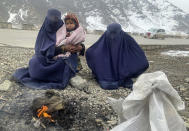 Gulnaz, left, keep her 18-month-old son warm themselves as they wait for alms in the Kabul - Pul-e-Alam highway eastern Afghanistan, Tuesday, Jan. 18, 2022. The Taliban's sweep to power in Afghanistan in August drove billions of dollars in international assistance out of the country and sent an already dirt-poor poor nation, ravaged by war, drought and floods, spiralling toward a humanitarian catastrophe. (AP Photo/Kathy Gannon)