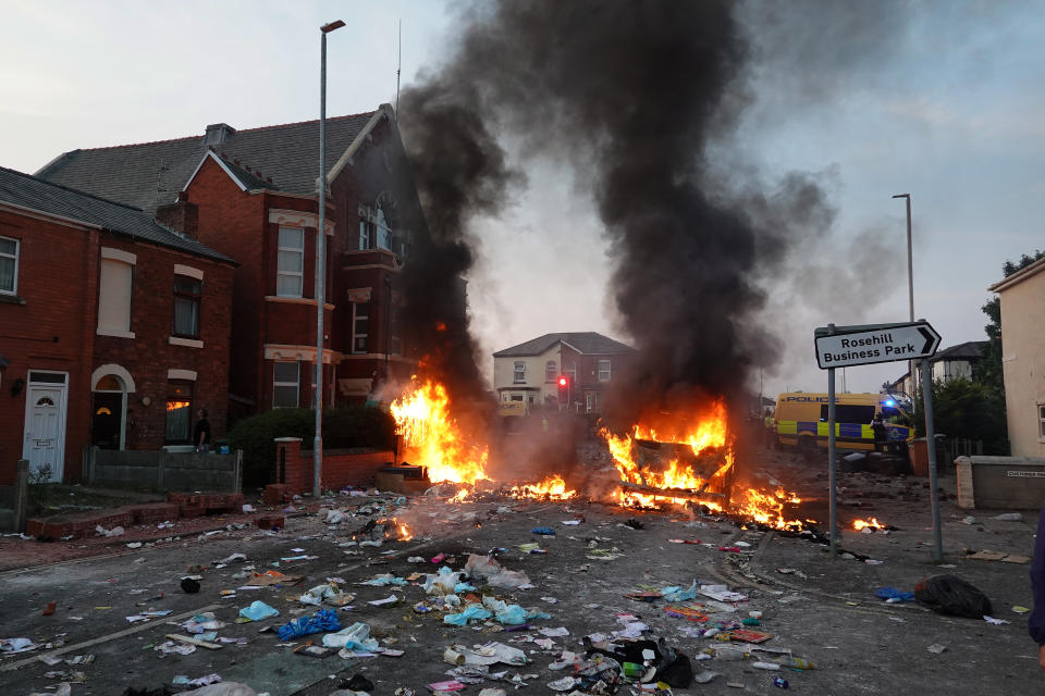 SOUTHPORT, ENGLAND - JULY 30: Riot police hold back protesters near a burning police vehicle after disorder broke out on July 30, 2024 in Southport, England. Rumours about the identity of the 17-year-old suspect in yesterday's deadly stabbing attack here have sparked a violent protest. According to authorities and media reports, the suspect was born in Cardiff to Rwandan parents, but the person cannot be named due to his age. A false report had circulated online that the suspect was a recent immigrant who crossed the English Channel last week and was 