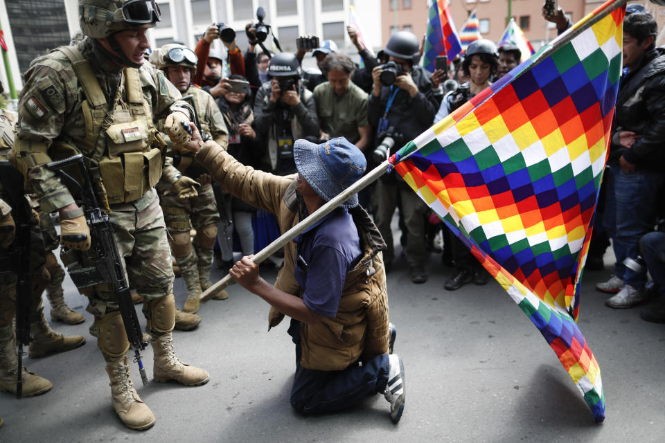 A backer of former President Evo Morales kneels in front of soldiers guarding a street in downtown La Paz, Bolivia, Friday, Nov. 15, 2019. Bolivia's new interim president Jeanine Anez faces the challenge of stabilizing the nation and organizing national elections within three months at a time of political disputes that pushed Morales to fly off to self-exile in Mexico after 14 years in power. (AP Photo/Natacha Pisarenko)