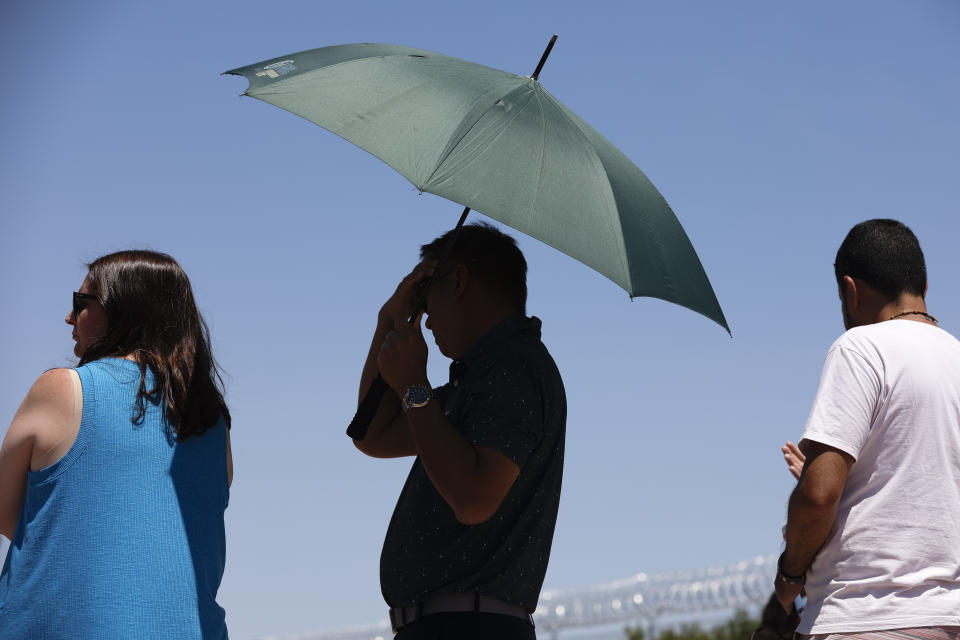 A person uses an umbrella to block the sun while waiting to take a photo at the "Welcome to Las Vegas" sign Monday, July 8, 2024, in Las Vegas. After causing deaths and shattering records in the West over the weekend, a long-running heat wave will again grip the U.S. on Monday, with hot temperatures also predicted for large parts of the East Coast and the South. (Wade Vandervort/Las Vegas Sun via AP)