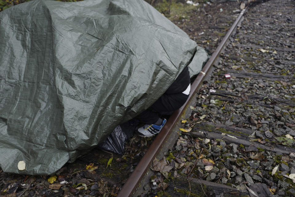 A migrant protects himself from the rain under a tarp in a makeshift camp in Calais, northern France, Saturday, Nov. 27, 2021. At the makeshift camps outside Calais, migrants are digging in, waiting for the chance to make a dash across the English Channel despite the news that at least 27 people died this week when their boat sank a few miles from the French coast. (AP Photo/Rafael Yaghobzadeh)