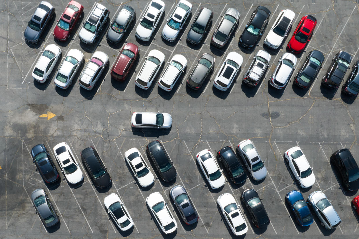 Vehicles arrayed in a parking lot, with regular empty spaces.