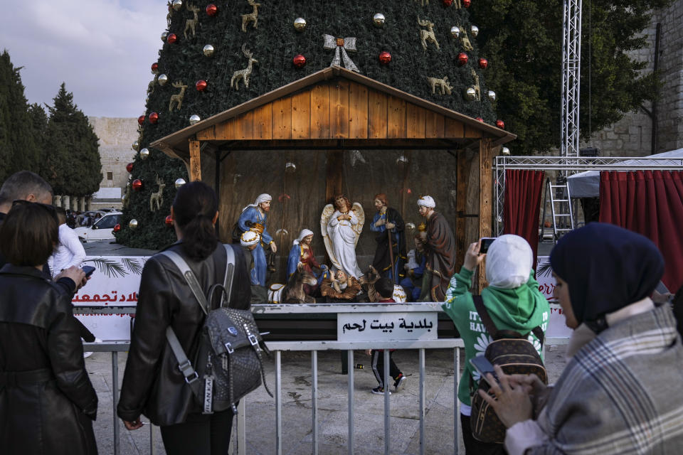 People take pictures of the Christmas tree and nativity scene in Manger Square, outside to the Church of the Nativity, traditionally believed by Christians to be the birthplace of Jesus Christ, ahead of Christmas, in the West Bank city of Bethlehem, Monday, Dec. 5, 2022. Business in Bethlehem is looking up this Christmas as the traditional birthplace of Jesus recovers from a two-year downturn during the coronavirus pandemic. Streets are already bustling with visitors, stores and hotels are fully booked and a recent jump in Israeli-Palestinian fighting appears to be having little effect on the vital tourism industry. (AP Photo/ Mahmoud Illean)