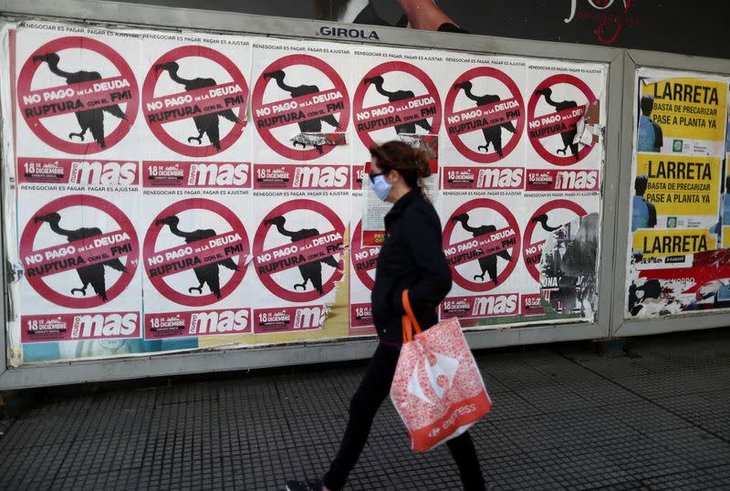 FILE PHOTO: A pedestrian wearing a protective face mask walks past posters on the street that read "No to the payment of the debt. Break with the IMF", in Buenos Aires