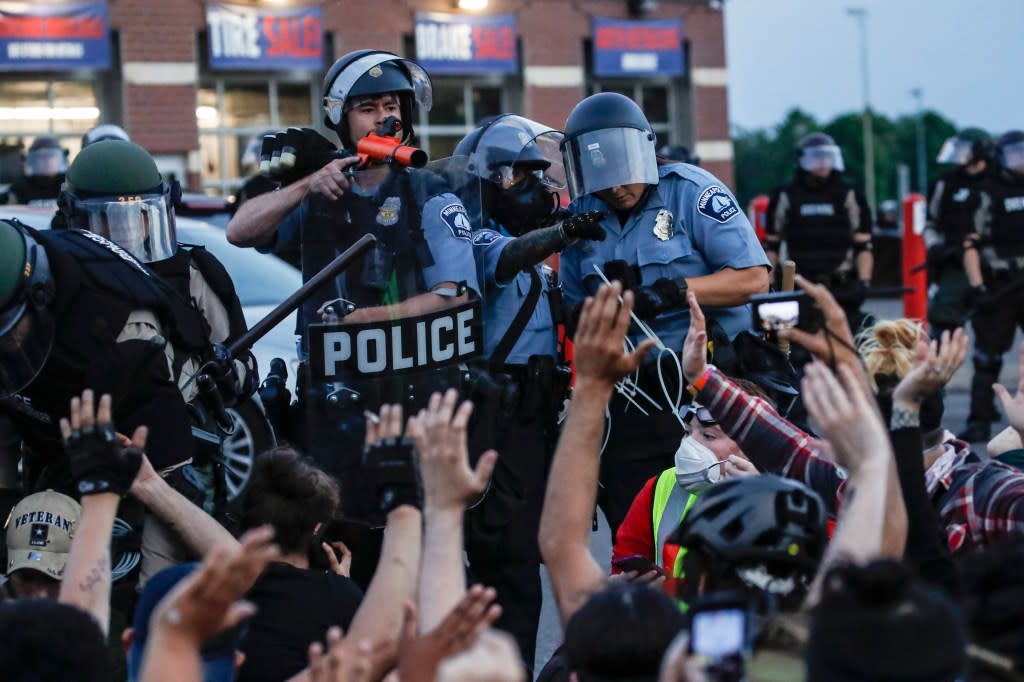 A police officer points a hand cannon at protesters who have been detained pending arrest on South Washington Street in Minneapolis, May 31, 2020, as protests continued following the death of George Floyd. (AP Photo/John Minchillo, File)