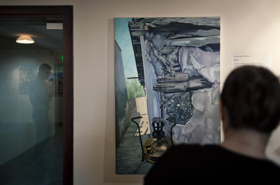 In this photo taken Saturday, May 10, 2014, a man looks at an acrylic on canvas painting by Palestinian artist Mohammed al-Madhoun named Housh, during an art exhibition "Traces, a testimony to memory," displaying over forty Palestinian artists work from Gaza, in the West Bank city of Ramallah. The Gaza Strip is tough turf for artists. An Israeli-Egyptian border blockade of the Hamas-ruled territory keeps them away from an international audience and potential buyers, while the local art market is close to nil. A new exhibit now offers them a chance to showcase their work outside Gaza. (AP Photo/Nasser Nasser)