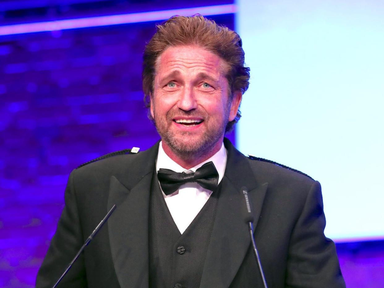 A man in a black tuxedo looks slightly alarmed while standing on a stage at a podium.