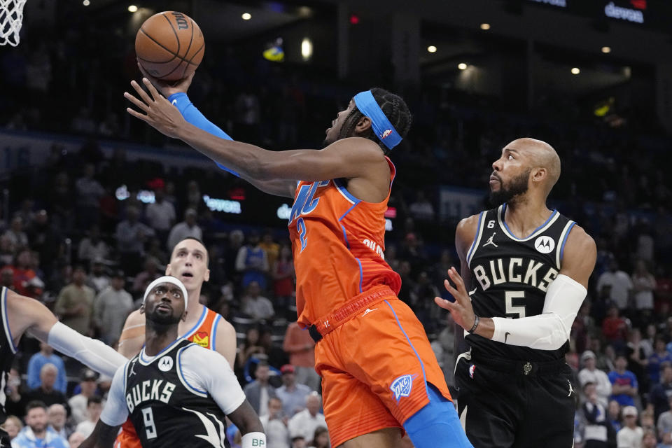 Oklahoma City Thunder's Shai Gilgeous-Alexander, center, goes to the basket between Milwaukee Bucks' Bobby Portis (9) and Jevon Carter (5) during the first half of an NBA basketball game Wednesday, Nov. 9, 2022, in Oklahoma City. (AP Photo/Sue Ogrocki)