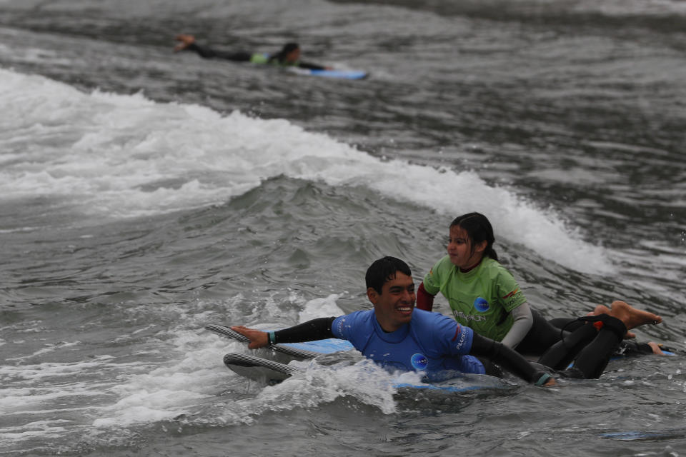 An instructor tows out a young student for a surf lesson at Barranquito beach in Lima, Peru, Thursday, July 25, 2019. Today, dozens of schools teach tourists from across the world how to ride waves at beaches with Hawaiian names in Lima's Miraflores district, while professional surfers from across the Americas prepare to compete when the sport is featured for the first time in the Pan American Games in the Peruvian capital.(AP Photo/Rebecca Blackwell)
