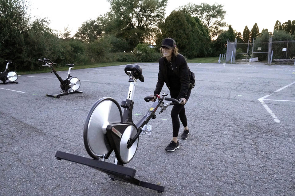 Jeanne Carter, co-owner of Fuel Training Studio, in Newburyport, Mass., removes stationary exercise bikes from a parking lot outside the gym following a spinning class, Monday, Sept. 21, 2020, in Newburyport. The gym's revenue is down about 60% during the COVID-19 pandemic. Fuel Training Studio plans to continue holding outdoor classes into the winter with the help of a planned greenhouse-like structure with heaters but no walls. (AP Photo/Steven Senne)