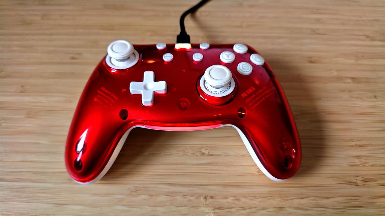  A Ruby red PB Tails Crush gaming controller sitting on a wooden desk. 