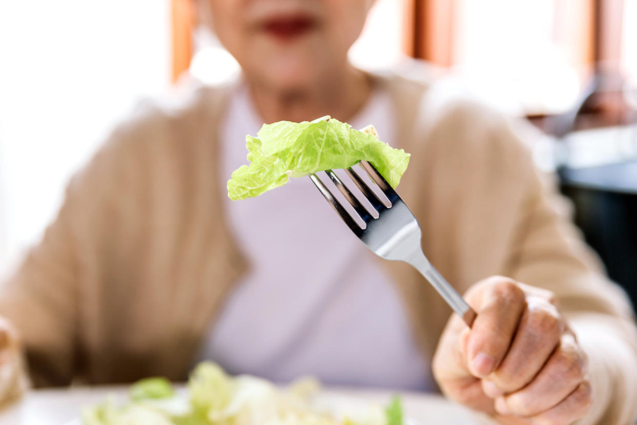 Close-up of fresh and clean lettuce Poke with a fork from a vegetarian salad served to a senior female patient at home. Caregiver visit at Home. Home health care concept and nursing home.