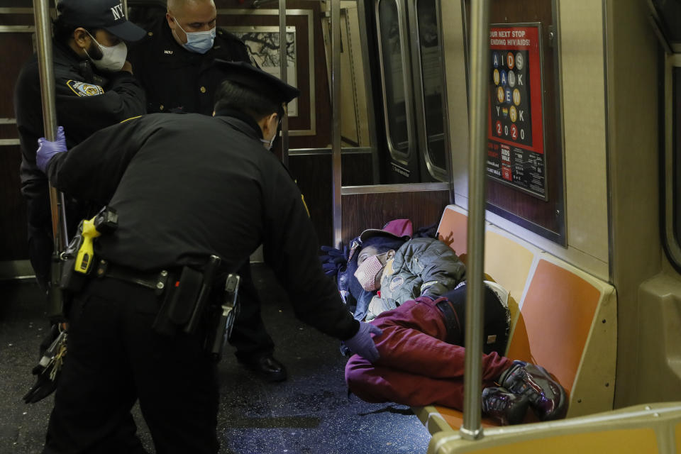 NYPD and MTA officers wake up a sleeping passenger before directing him to exit the 207th Street A-train station, Thursday, April 30, 2020, in the New York. (AP Photo/John Minchillo)