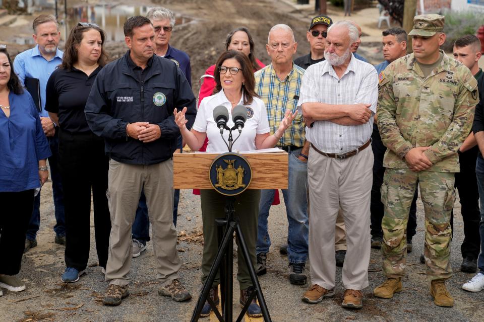 Governor Kathy Hochul, center, alongside an entourage of emergency workers and officials, speaks to members of the media on a floodwater-damaged Main Street, Monday, July 10, 2023, in Highland Falls, N.Y. Heavy rain has washed out roads and forced evacuations in the Northeast as more downpours were forecast throughout the day. One person in New York's Hudson Valley has drowned as she was trying to leave her home. (AP Photo/John Minchillo)