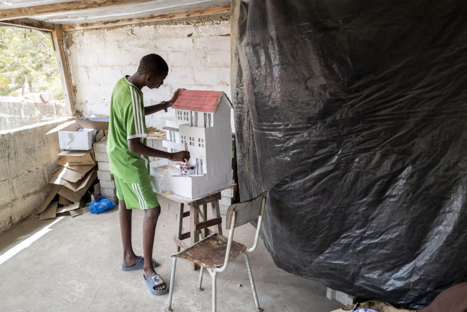 Mouhamed Sall, who is deaf, and known for his talent for drawing and manual activities, paints a small house he built in Pikine, Senegal, Monday, March 18, 2024. Sall and three other students are part of a new approach in a small number of schools in Senegal that seat those who are deaf and hard of hearing with the rest of the class. (AP Photo/Sylvain Cherkaoui)