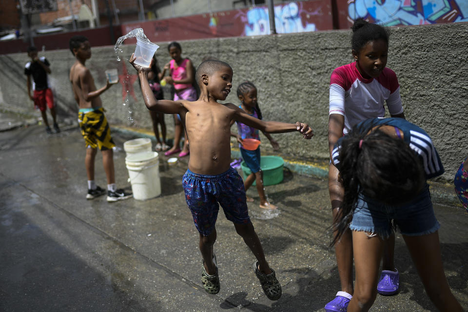 A boy prepares to playfully drench a friend with water during carnival celebrations in the Pinto Salinas neighborhood of Caracas, Venezuela, Monday, Feb. 15, 2021, amid the new coronavirus pandemic. (AP Photo/Matias Delacroix)