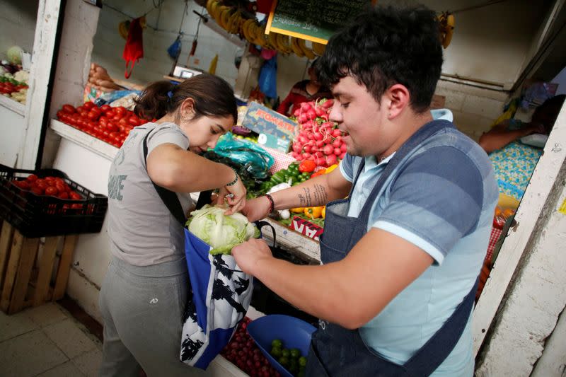 A vendor helps a woman to arrange items in a bag at a market which no longer provides plastic bags for customers to carry products, in Mexico City