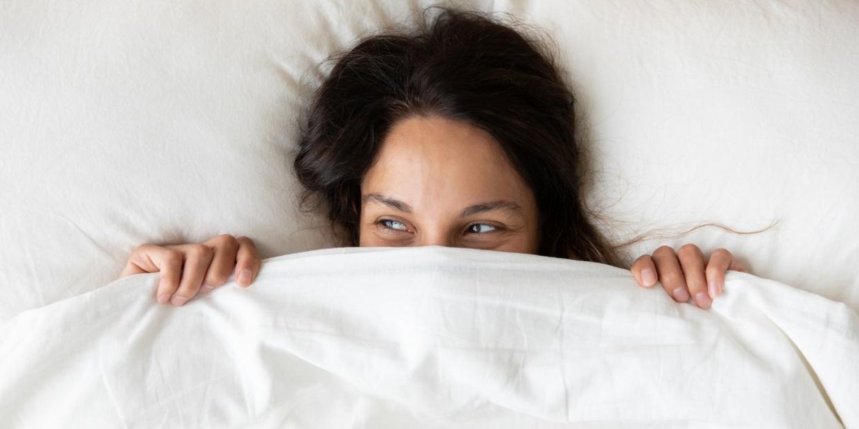 above view playful young woman hiding face under blanket