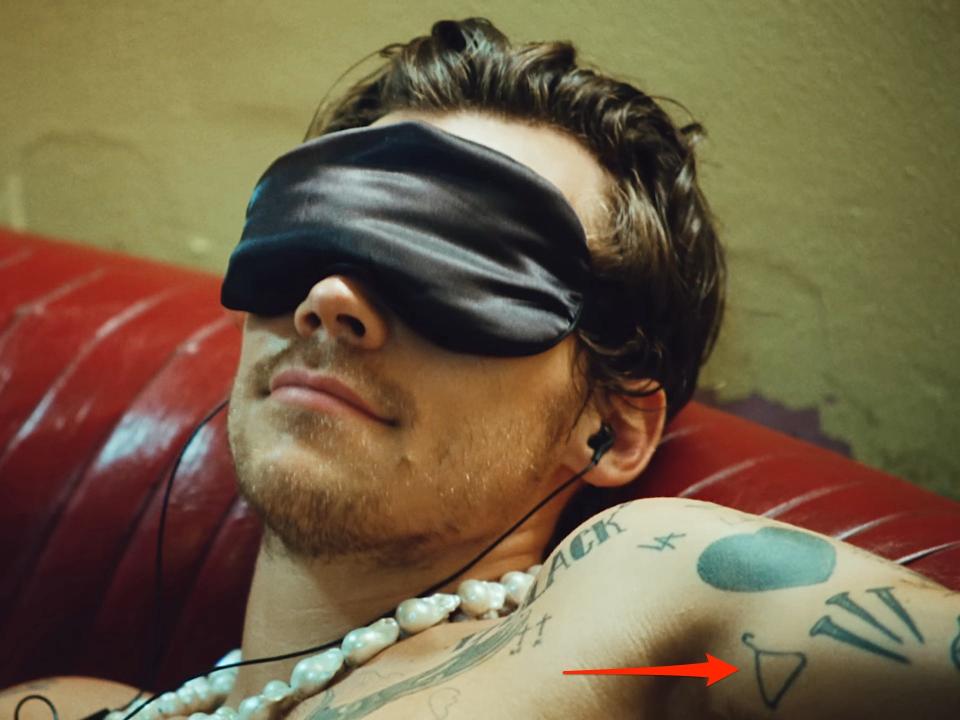 A red arrow pointing to a coat hanger tattoo, seen in Harry Styles' music video for "Music for a Sushi Restaurant."