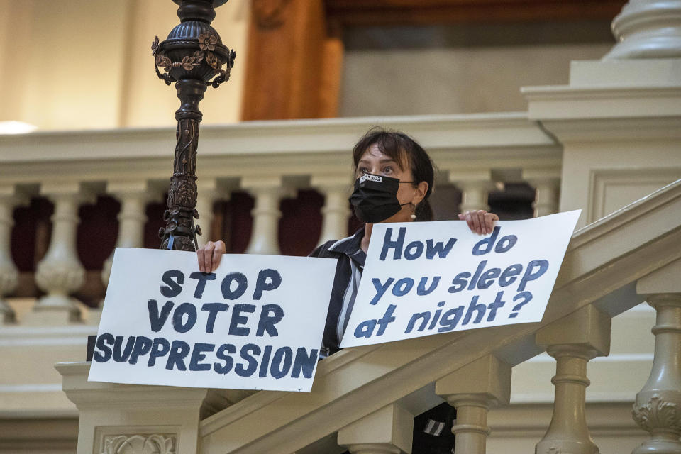 Ann White of Roswell holds protest signs on the North Wing stairs of the Georgia State Capitol building on day 38 of the legislative session in Atlanta, Thursday, March 25, 2021. 