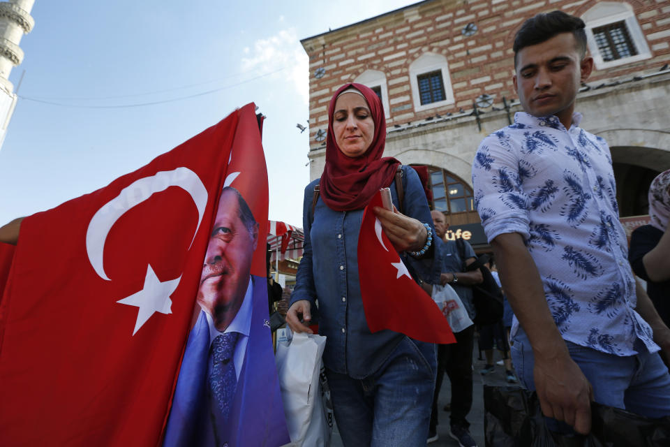 People walk past a street vendor offering Turkish flags for sales at a market in Istanbul, Thursday, Aug. 16, 2018. Beset by a weak currency and tension with the United States, Turkey is reaching out to Europe in an attempt to shore up relations with major trading partners despite years of testy rhetoric and a stalled bid for EU membership. The overtures by Turkish President Recep Tayyip Erdogan, who has harshly criticized Germany and other European nations in the past, are part of a diplomatic campaign to capitalize on international unease over U.S. President Donald Trump and American tariff disputes. (AP Photo/Lefteris Pitarakis)