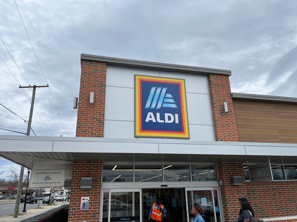 An einem bewölkten Tag in Hyattsville, Maryland, betreten und verlassen die Menschen einen Aldi-Lebensmittelmarkt. Das blau-weiße Aldi-Logo prangt auf einem Schild über dem Eingang, während links vom Eingang eine Reihe von Einkaufswagen steht.