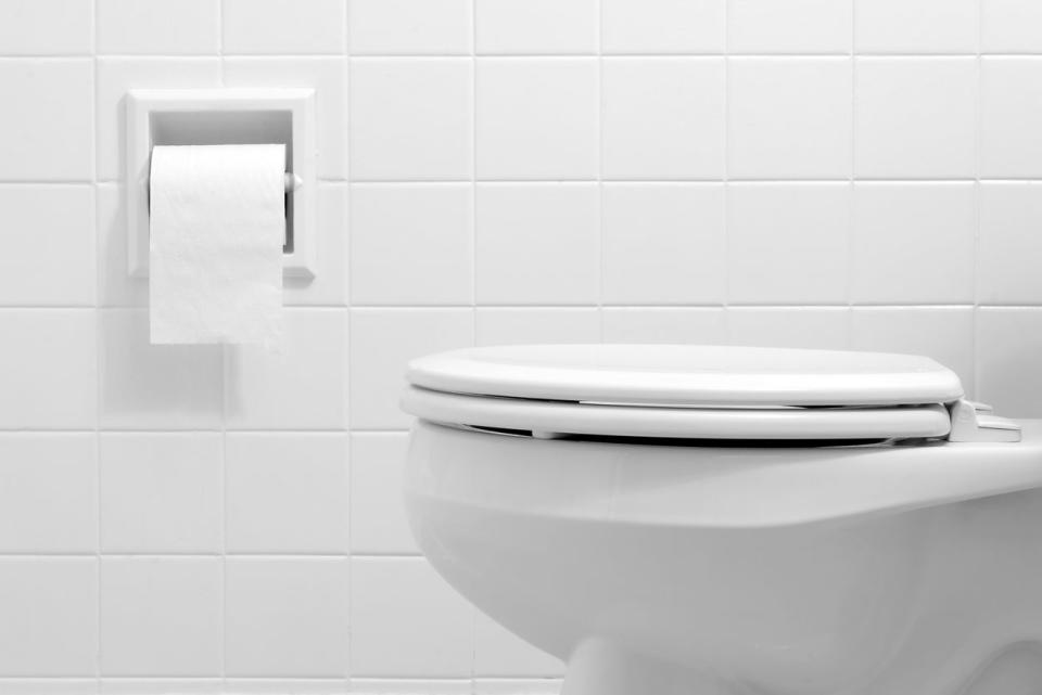 A closed toilet next to toilet paper in a white tile bathroom.