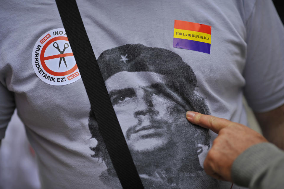 A citizen shows a portrait of ''Che Guevara'' in a shirt of one demonstrator between two stickers against the Spanish Government's cutback plans, and for a new Spanish Republic, right, in Pamplona, northern Spain, Sunday, Oct. 7, 2012. Thousands of people called by 150 organizations are marching in 56 Spanish cities to protest punishing austerity cuts they say will only increase unemployment and job insecurity. (AP Photo/Alvaro Barrientos)