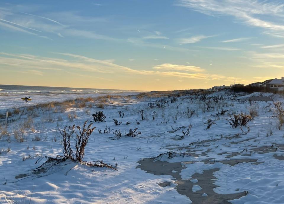 Snow on a Surf City beach during the winter of 2022. Two surfers walk towards the water to catch some cold waves.