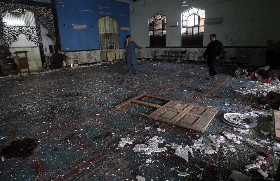 Man talks on a mobile phone while another walks amidst debris after an explosion in a Shi'ite mosque in Peshawar