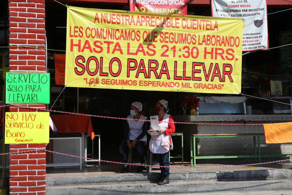 Restaurant workers wait for customers at a restaurant open only for take away service in Mexico City, Sunday, Dec. 20, 2020. After months of resisting to avoid hurting the economy, officials banned all non-essential activities starting Saturday and returned to a partial lockdown in Mexico City and the surrounding State of Mexico because of a spike in coronavirus cases that has crowded hospitals. (AP Photo/Ginnette Riquelme)