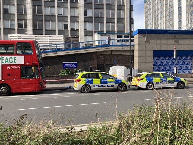 Two parked police cars and a red double decker bus with a forensic tent in the background.