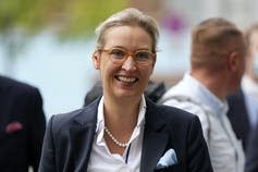  A woman smiling in a blazer, glasses and pearls.