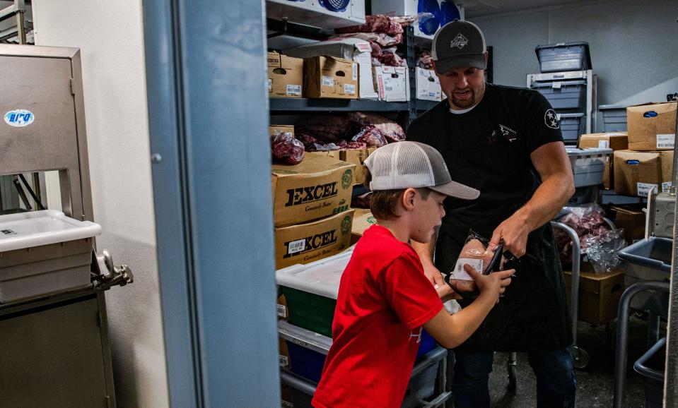 Casey Weber, right, hands his son Jack chicken breast to be stocked on the shelves at Tallgrass Meat Co. in Columbia, Tenn. on Monday July 18, 2022.