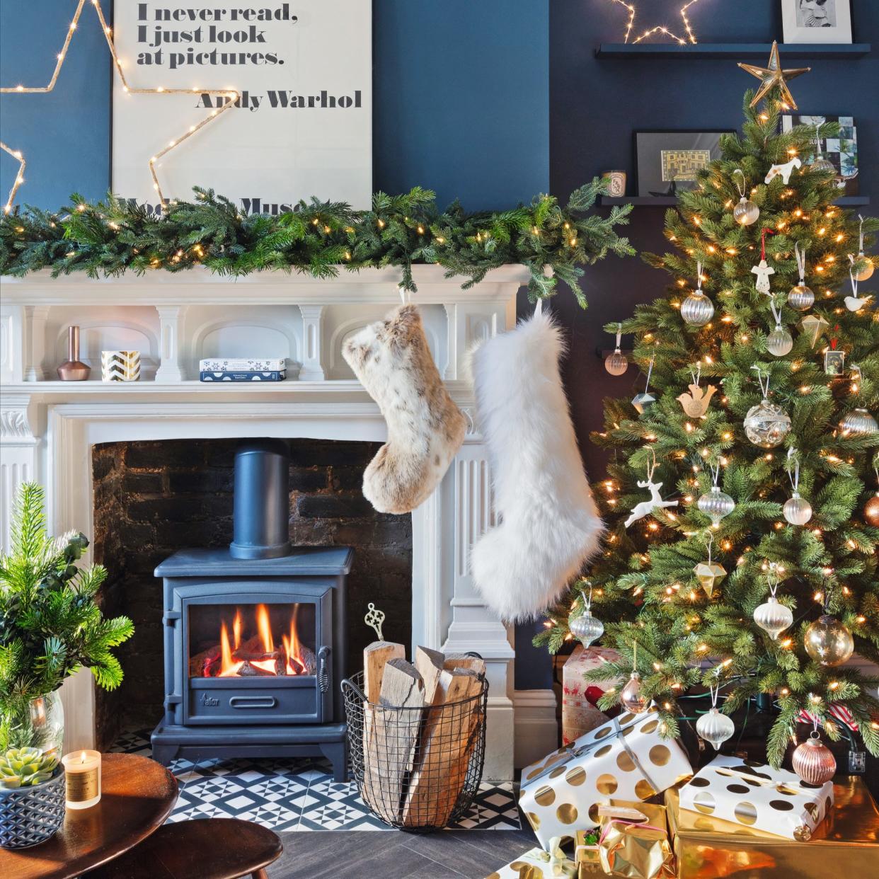  Christmas tree with presents on the floor, next to traditional fireplace with stockings. 