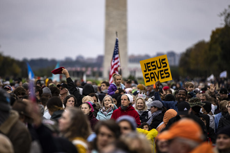 People, mainly women, mill around in front of the National Monument, one holding a sign saying: Jesus Saves.