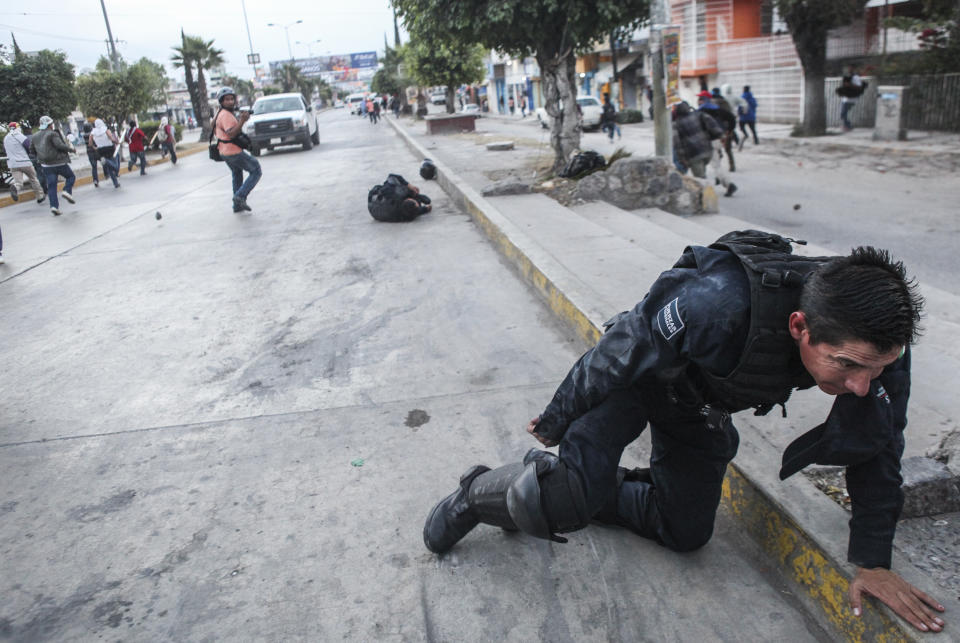 In this Dec. 2014 handout photo provided by Cristopher Rogel Blanquet, a federal police officer attempts to pull himself up onto a sidewalk after being injured in a clash with protesters in Chilpancingo, Mexico. This photo was not taken in confrontations with migrants making their way in a caravan from Central America to the U.S., despite a post circulating on social media. (Photo by Cristopher Rogel Blanquet via AP)