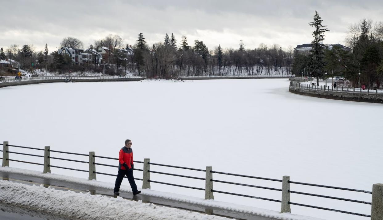 A pedestrian walks alongside the Rideau Canal in Ottawa on Jan. 10, 2024. The skateway was only open for a few days this winter, and remains closed. (Adrian Wyld/The Canadian Press - image credit)