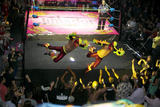 In this Wednesday, Feb. 12, 2014 photo, wrestling duo The Crazy Chickens fly over the ropes and into the audience during the Lucha VaVoom Valentine’s show of Lucha Libre Mexican wrestling and Burlesque performances at the Mayan Theatre downtown Los Angeles. The esoteric hybrid of American burlesque and Mexican wrestling is an outrageous hit.(AP Photo/Damian Dovarganes)