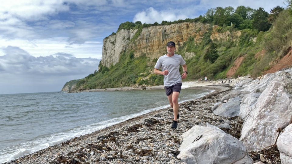 The reviewer running along a beach wearing the Buff 5-Panel Air Cap