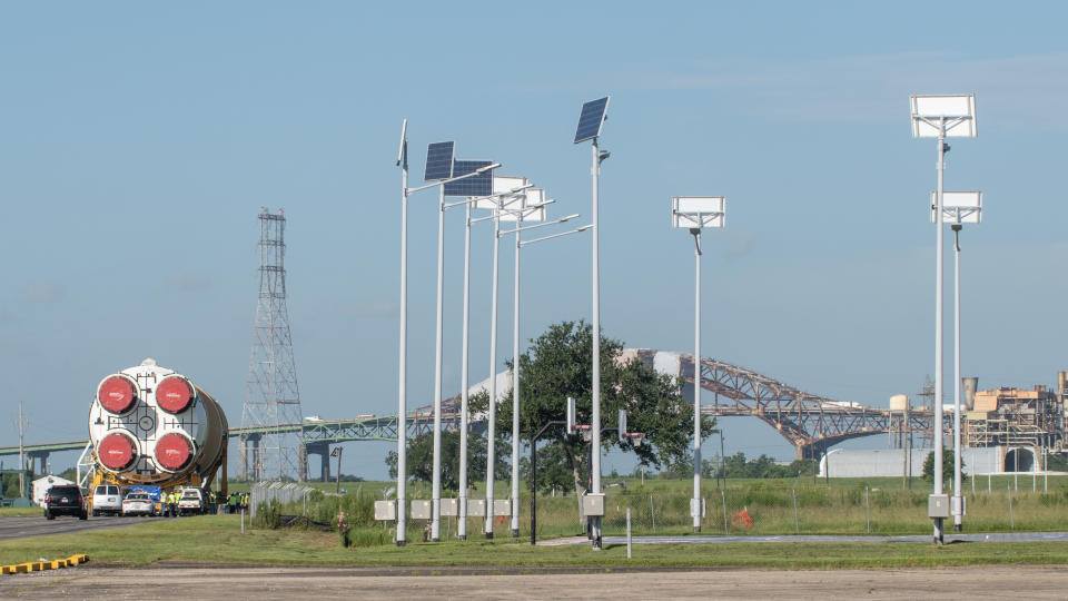 We see the butt of a rocket booster with four cowlings covered in red canvas slowly moving toward a tubular boat seen in the distance to the right.