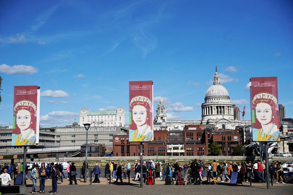 Signs with a photo of the Queen and "In tribute to HM Queen Elizabeth II" text above the crowd