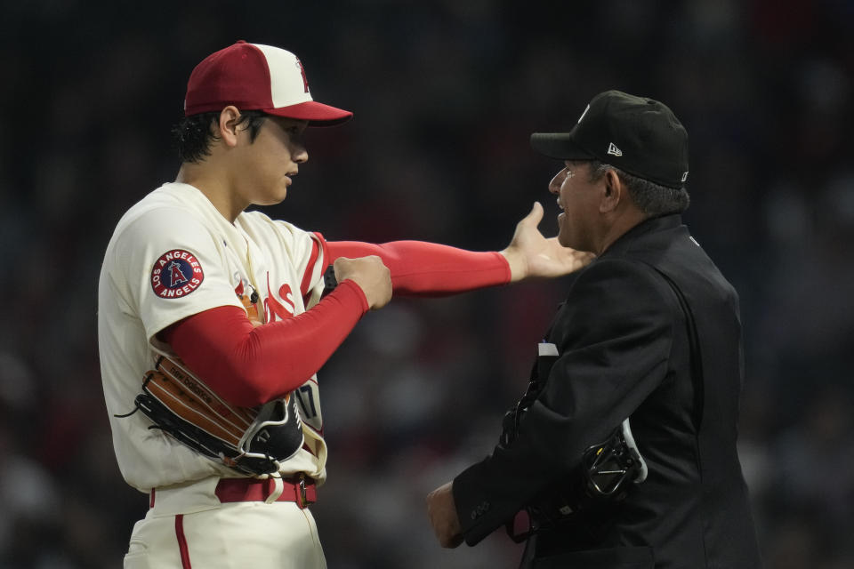 Umpire Alfonso Marquez, right, inspects a pitch calling device on the left arm of Los Angeles Angels starting pitcher Shohei Ohtani (17) in the middle of the fifth inning of a baseball game against the Washington Nationals in Anaheim, Calif., Tuesday, April 11, 2023. (AP Photo/Ashley Landis)